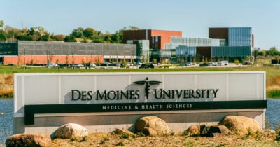 A sign displaying the Des Moines University logo, with the campus in the background.