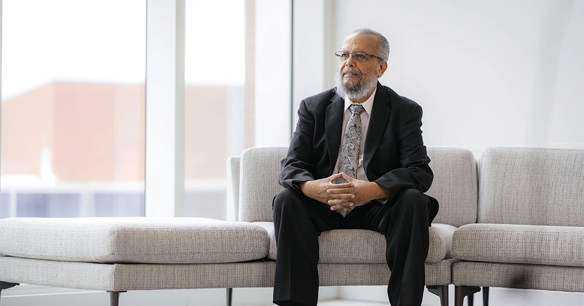 Simon Geletta, Ph.D., seated on a couch as he poses for a photo.