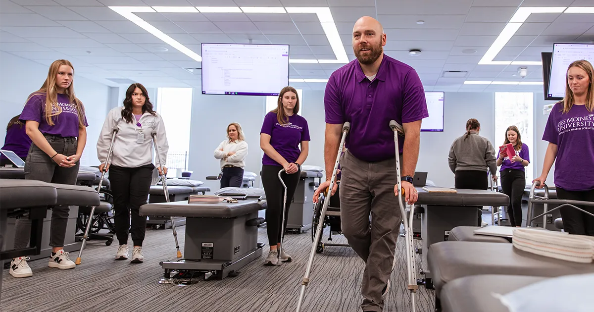 Occupational therapy students and an instructor using crutches and adaptive equipment in a clinical lab setting to practice mobility techniques.