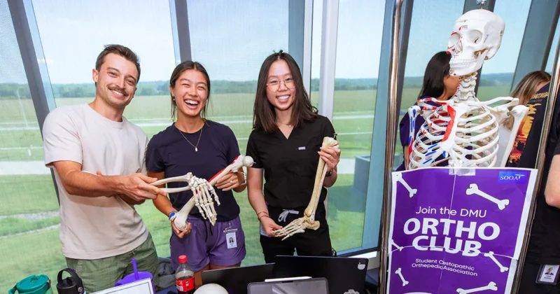 Students at DMU’s annual Club Day staffing a table for the Student Osteopathic Orthopedic Association, smiling and holding bone models alongside a skeleton display and “Join the DMU Ortho Club” sign.