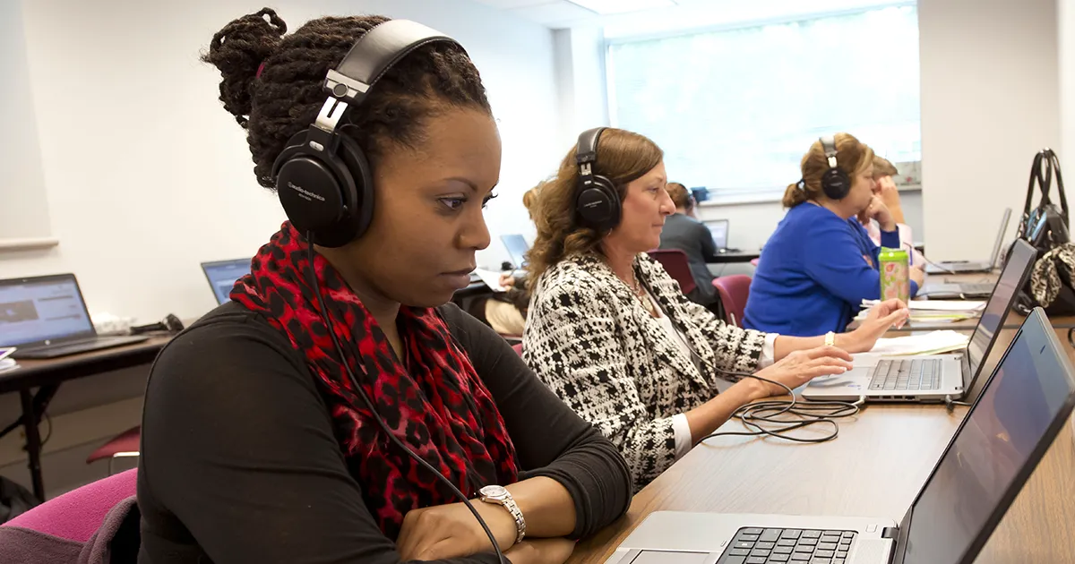 MHA students sit in a classroom working on laptops while wearing headphones, participating in a guided learning activity.