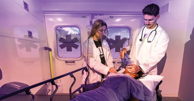 Two students use a bag valve mask to provide simulated care to a patient on a stretcher at the Regional Simulation Center at DMU32.