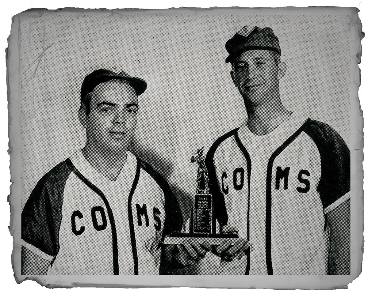 Two COMS baseball players in vintage uniforms holding a small trophy.