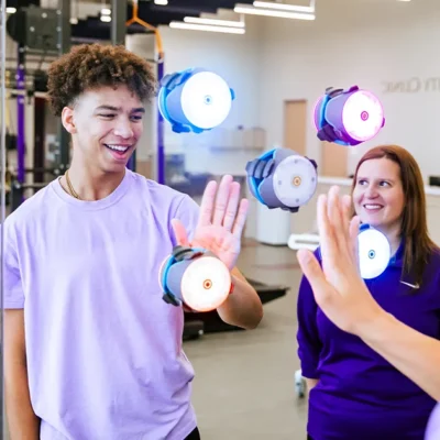 A patient participates in a reaction‑time activity, reaching toward several wall‑mounted lights inside a clinical or training facility.