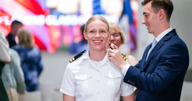 Scene from Des Moines University’s Military Commissioning Ceremony for graduates entering into military medical service. A graduate in US Navy garb receives a pin on her lapel.