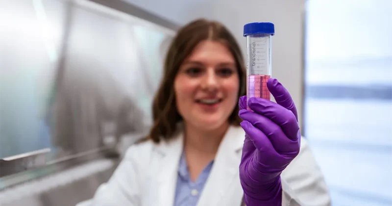 A DMU student researcher inspects a vial of pink liquid.