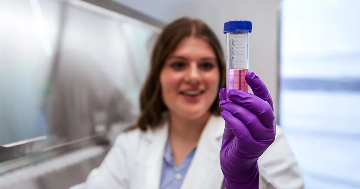 A DMU student researcher inspects a vial of pink liquid.