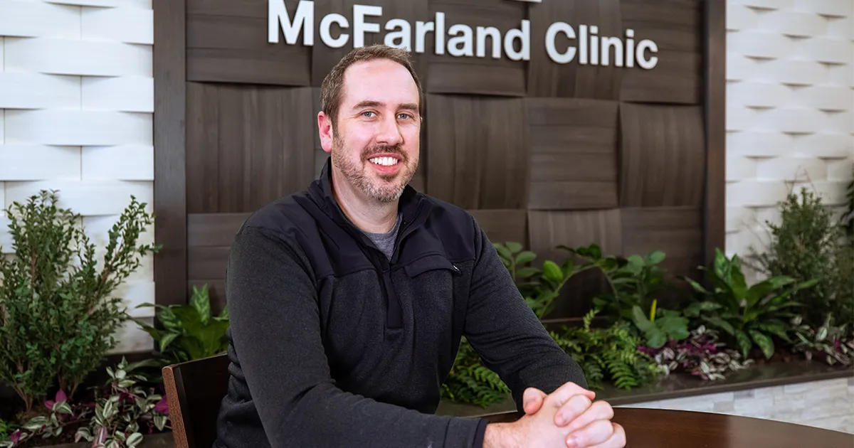 Jeffrey Dikis, DPM’12, sits at a table in the McFarland Clinic atrium with a landscaped indoor garden in the background.