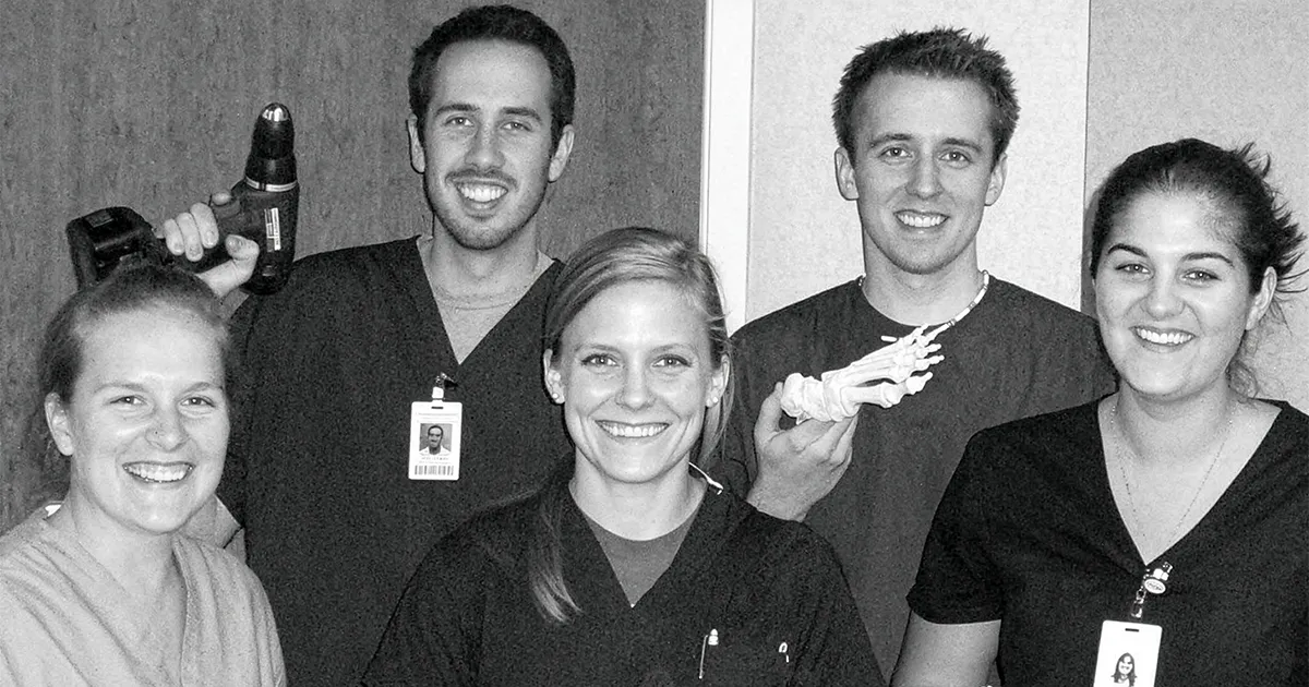 Jeffrey Dikis, DPM’12, stands with fellow podiatric medical students in clinical attire, with a foot model displayed during a training activity.