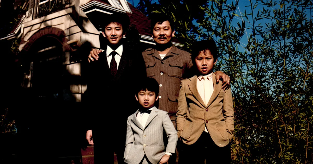 Childhood photo of John T. Pham with his father and two brothers standing outdoors in front of a house.