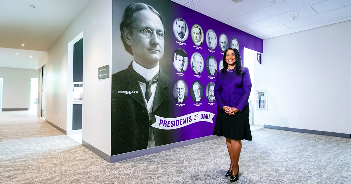 DMU President Angela L. Walker Franklin stands in front of a campus display featuring portraits of DMU's 14 previous presidents, including founder Summerfield Saunders Still.