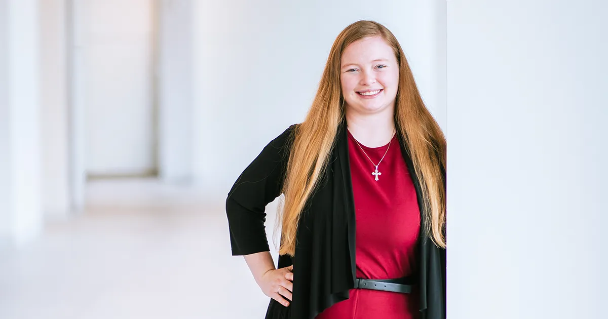 Kassidy Hackbarth, OTD’26, stands in a campus hallway wearing a red outfit and black cardigan