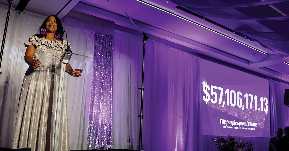 President Angela L. Walker Franklin, PhD, stands at a podium during the Purple & Proud Finale as a large screen displays the campaign total of $57,106,171.13.