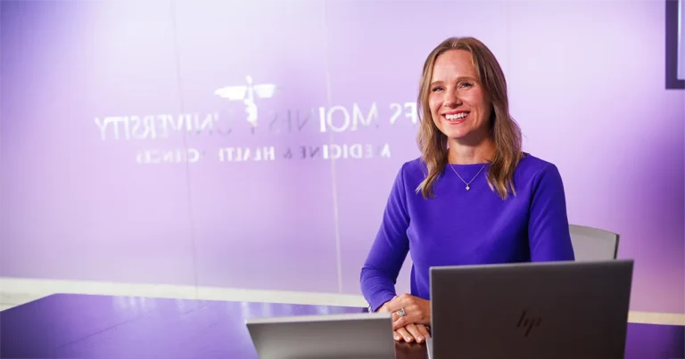 Rachel Reimer, PhD, sits at a conference table with a laptop in a meeting room at Des Moines University Medicine and Health Sciences.