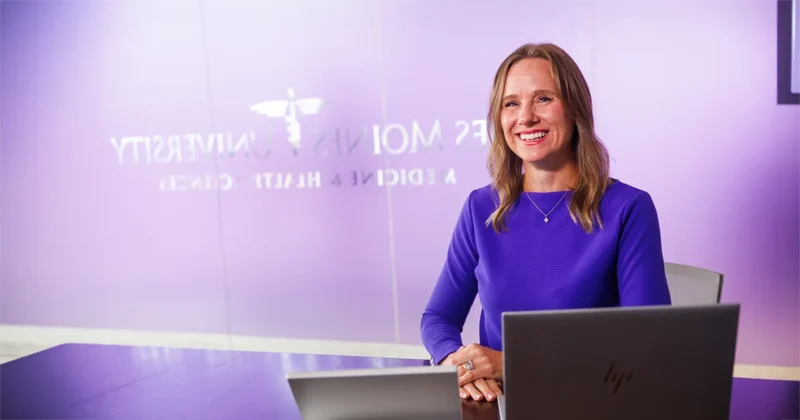 Rachel Reimer, PhD, sits at a conference table with a laptop in a meeting room at Des Moines University Medicine and Health Sciences.