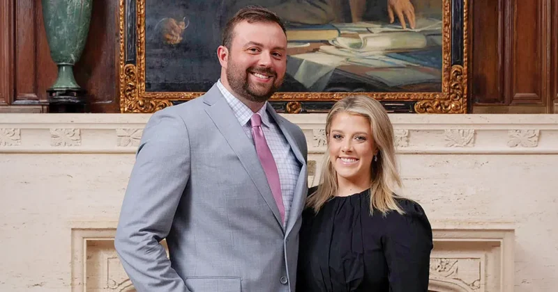 Austin Teel, DO’24, MSBS’20, stands beside his significant other in a formal interior with a stone fireplace and framed painting in the background.