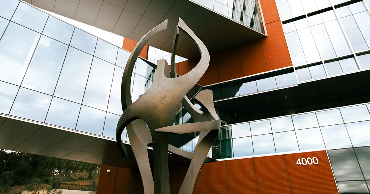 View of “The Gathering” sculpture in The Plaza, framed by the glass exterior of DMU’s academic buildings.