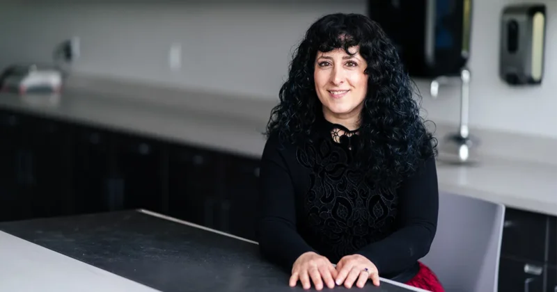 Julie Meachen, PhD, professor of anatomy, seated at a lab bench in a teaching laboratory with cabinets and work surfaces visible in the background.
